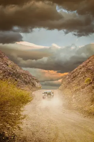 Voiture type 4x4 blanche roulant sur une route de terre entourée de roches