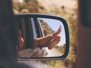 Vue sur des pieds qui dépassent d'une fenêtre de voiture dans un rétroviseur