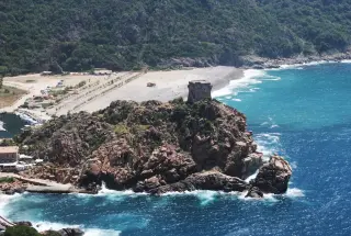 Plage de sable en Corse avec des rochers et un édifice
