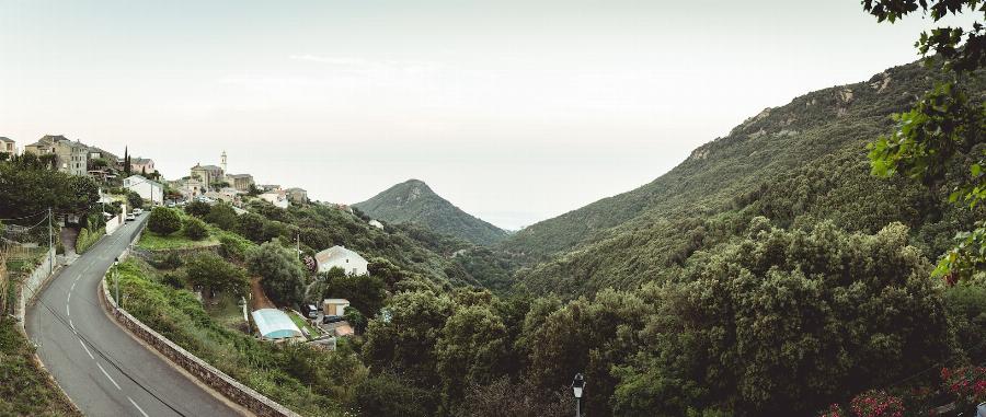Route longeant un village niché en haut d'une montagne boisée en Corse