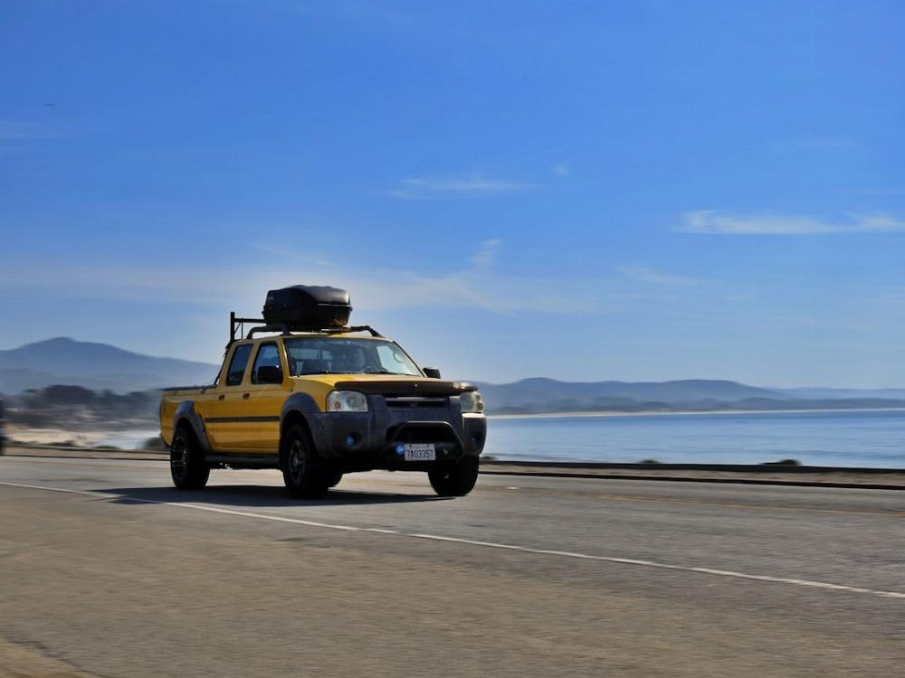 Voiture type 4x4 jaune roulant sur une route en bord de mer