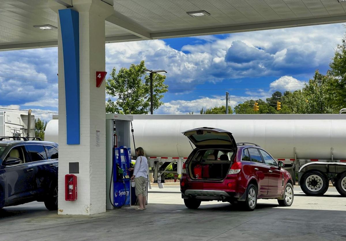 Une femme et une voiture rouge avec le coffre ouvert dans une station essence