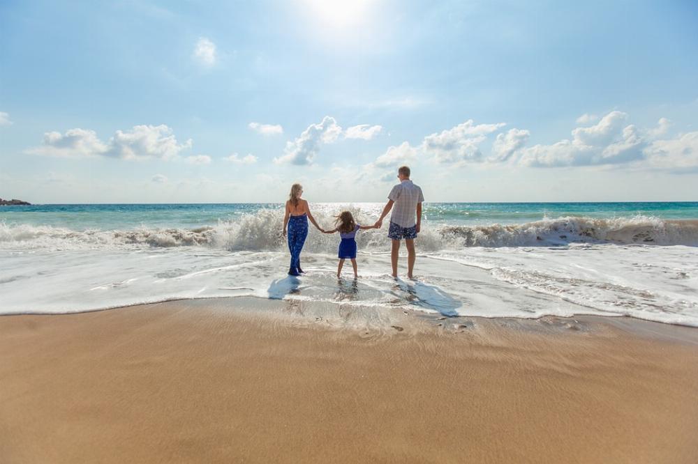 Un couple et leur enfant sur une plage les pieds dans la mer