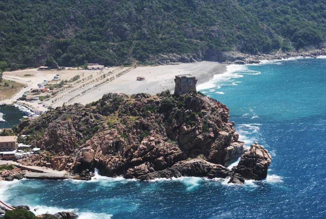 Plage de sable en Corse avec des rochers et un édifice