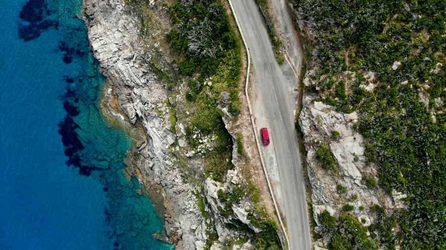 Vue aérienne d'une voiture rouge sur une route en Corse en bord de mer