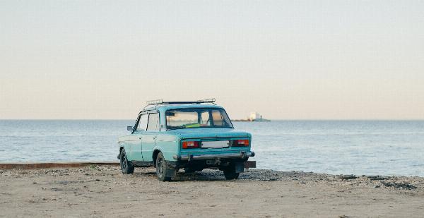 Une voiture bleue garée sur une plage de sable devant la mer